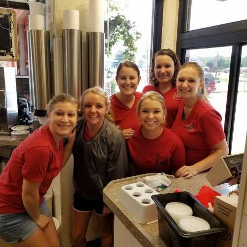A group of six smiling women in red shirts pose together at a restaurant counter.