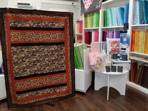 A colorful quilt displayed in a fabric store, surrounded by various fabric rolls and crafting supplies.