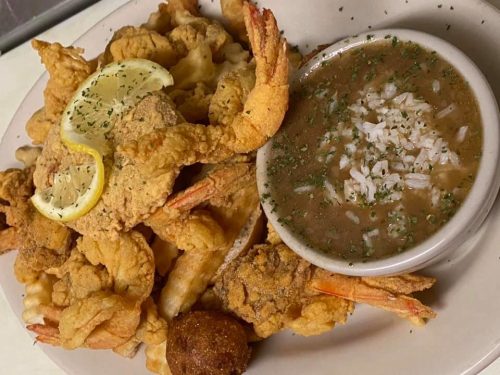 A plate of fried shrimp and seafood with a side of gumbo and rice, garnished with parsley and lemon slices.