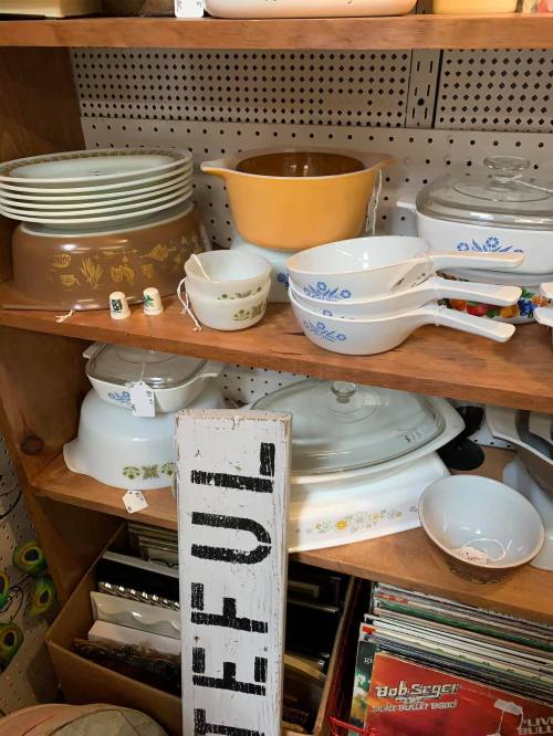 A shelf filled with vintage kitchenware, including bowls, pots, and a decorative sign that reads "Grateful."