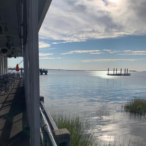 A serene waterfront view with calm water, a distant dock, and a clear sky reflecting sunlight.