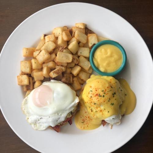 A plate of eggs Benedict with two poached eggs, hollandaise sauce, and crispy potatoes on the side.
