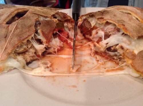 A freshly cut calzone filled with melted cheese, meats, and sauce, resting on a plate with a knife beside it.