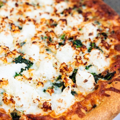 Close-up of a cheesy pizza topped with dollops of ricotta and spinach, featuring a golden, crispy crust.