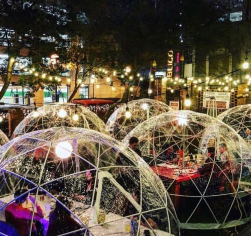 A cozy outdoor dining area with transparent igloo-like structures, illuminated by string lights at night.