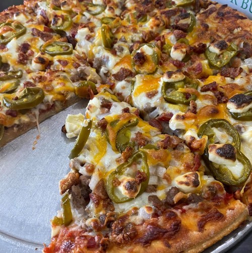 A close-up of a pizza topped with cheese, jalapeños, bacon, and sausage, served on a metal tray.