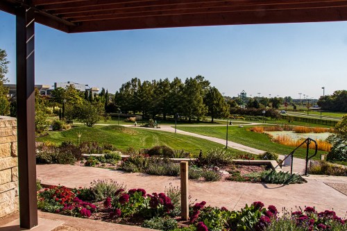 A scenic view of a landscaped park with colorful flowers, trees, and a clear blue sky in the background.