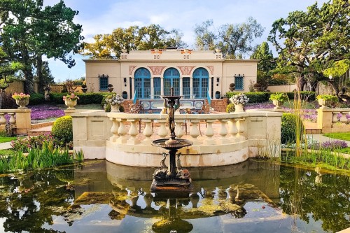 A beautiful garden with a fountain, surrounded by colorful flowers and a charming building in the background.