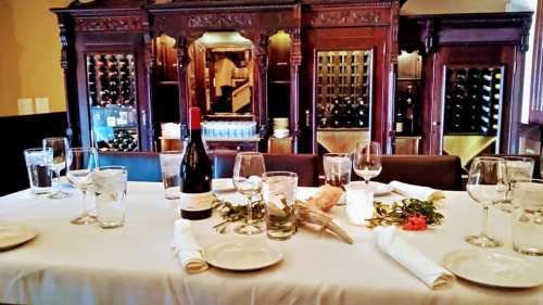Elegant dining table set with wine, glasses, and a floral centerpiece, against a backdrop of wooden wine cabinets.