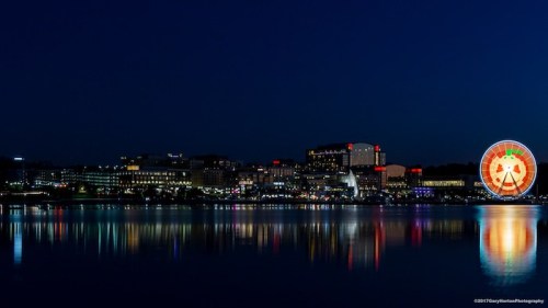 City skyline at night with colorful lights reflecting on the water, featuring a large Ferris wheel.