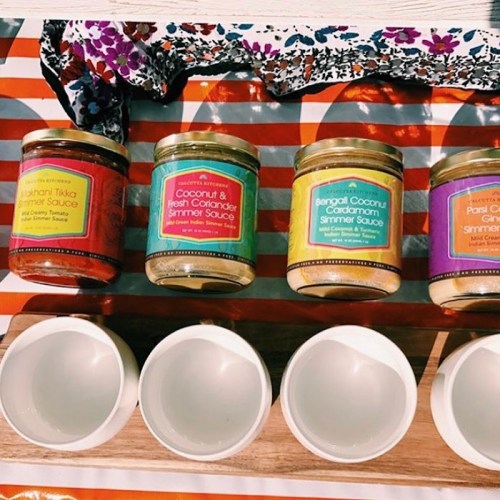 Four jars of simmer sauces on a striped tablecloth, with empty white bowls in front.