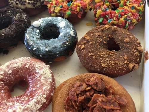 A variety of colorful donuts, including chocolate, fruity, and glazed, arranged in a box.