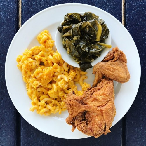 A plate with fried chicken, macaroni and cheese, and collard greens on a wooden table.