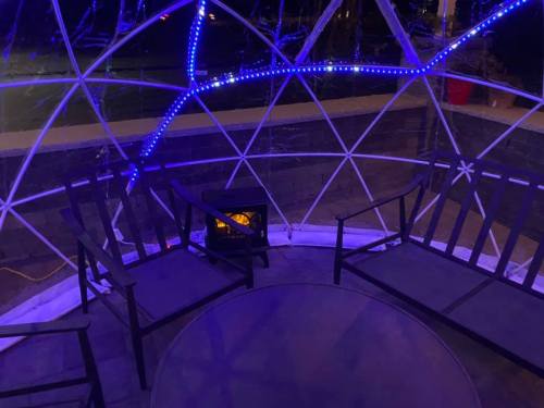 A cozy outdoor seating area inside a geodesic dome, featuring blue LED lights and a small heater.