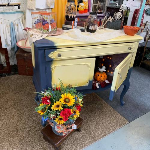 A vintage dresser with a yellow top and blue base, decorated with flowers and a small pumpkin inside.