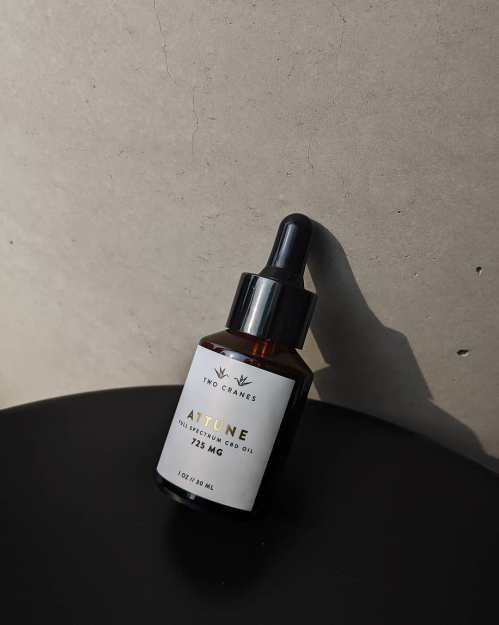 A brown glass dropper bottle of Attune oil with a white label, resting against a textured wall.