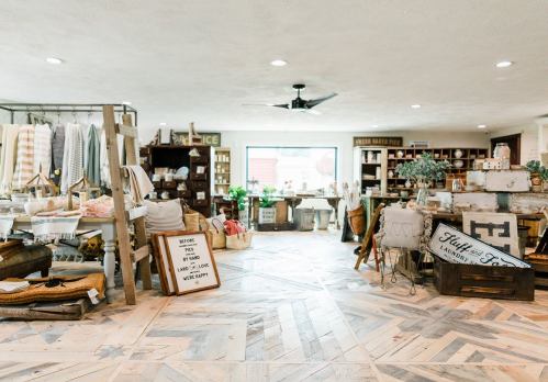A cozy shop interior featuring rustic decor, wooden shelves, and various home goods displayed on a patterned floor.