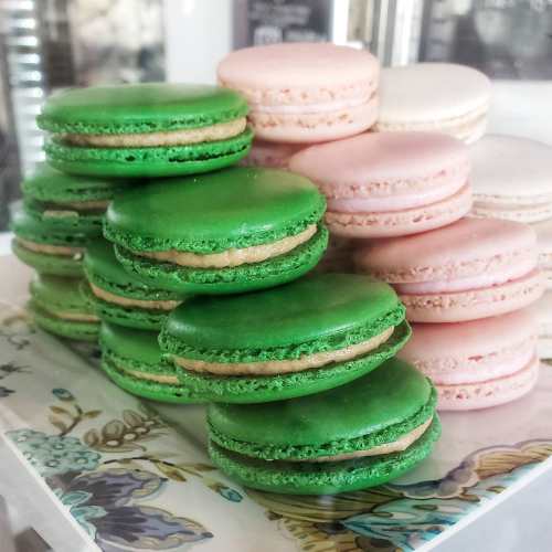 A plate of colorful macarons, featuring green and pink varieties stacked together.