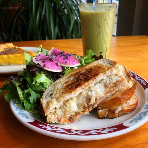 A toasted sandwich filled with sauerkraut, served with a side salad and a glass of iced green drink.