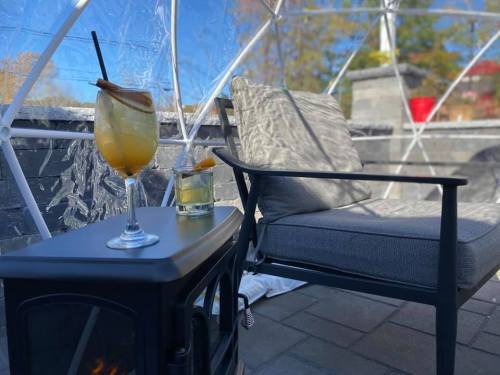 A cozy outdoor seating area with a drink on a table, a chair, and a small heater inside a clear dome.