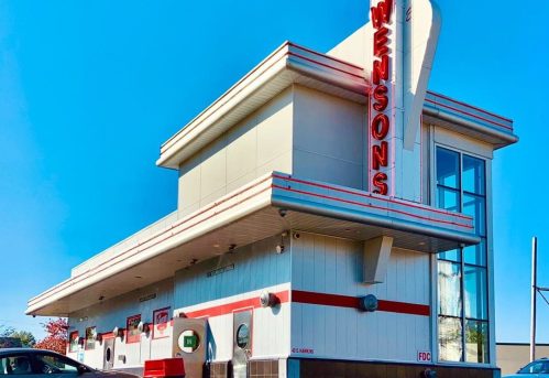 A retro-style fast food restaurant with a bright blue sky in the background, featuring a prominent sign that reads "Swenson's."