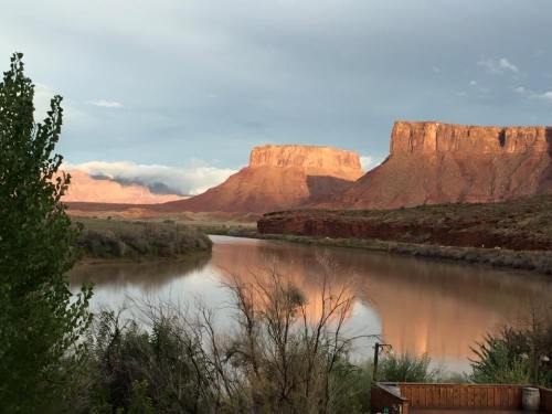 Scenic view of a river reflecting red rock formations under a cloudy sky, surrounded by greenery.