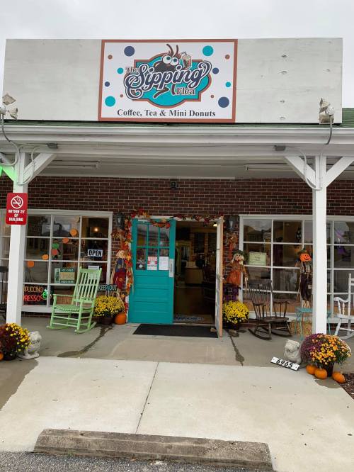 A cozy coffee shop entrance with a sign, colorful decor, and fall flowers outside.