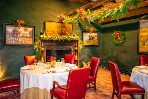 Cozy dining room with red chairs, festive decorations, and paintings, featuring a fireplace and elegant table settings.