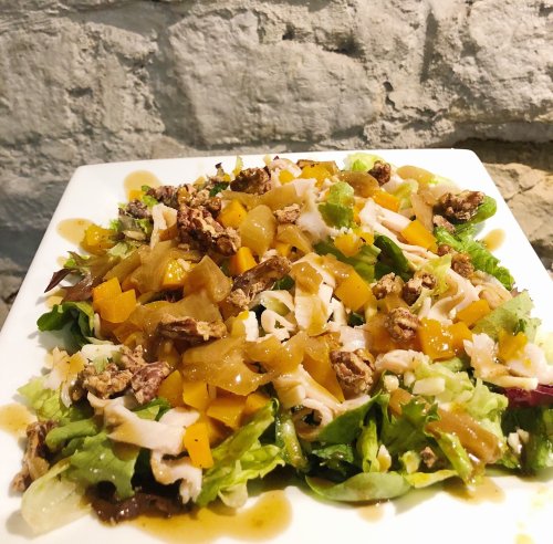 A colorful salad with mixed greens, diced vegetables, nuts, and a drizzle of dressing on a white plate.