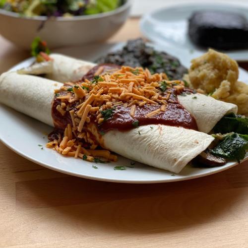 A plate of two enchiladas topped with red sauce and cheese, served with black beans and a side of mashed potatoes.