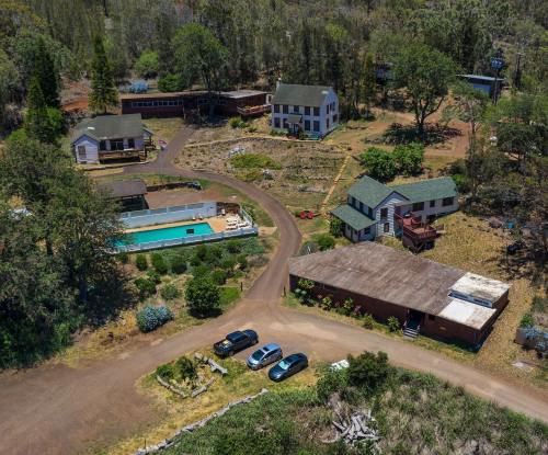 Aerial view of a rural property featuring multiple buildings, a pool, and parked cars surrounded by greenery.