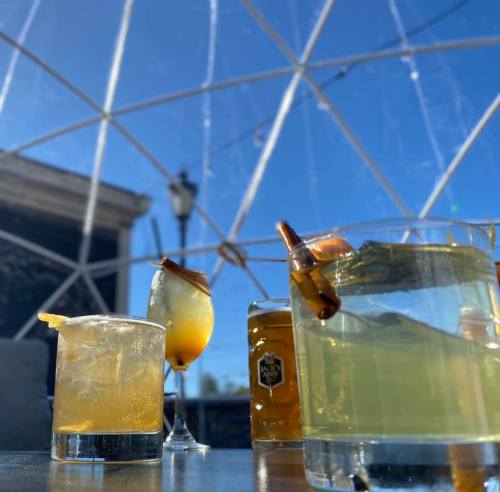 A close-up of various cocktails on a table, with a clear dome structure and blue sky in the background.