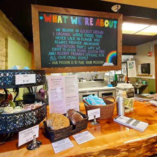 A café menu board highlighting organic, vegan, and gluten-free options, with baked goods displayed on the counter.