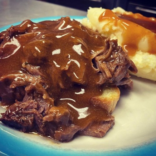 A plate featuring tender beef covered in brown gravy, served on bread with a side of mashed potatoes and gravy.