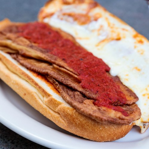 A sandwich with layers of fried meat and marinara sauce on a toasted hoagie roll.