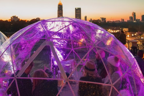 A group of people inside a glowing dome with a city skyline at sunset in the background.
