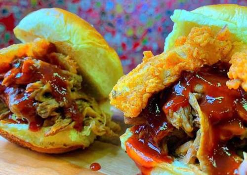 Close-up of two pulled pork sandwiches topped with barbecue sauce and crispy onion rings on soft buns.