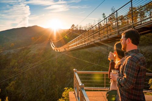 A couple enjoys drinks while watching the sunset from a bridge overlooking a valley.