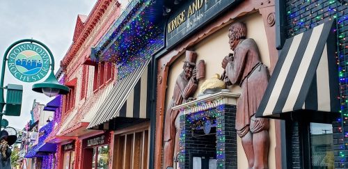 Colorful storefronts adorned with holiday lights, featuring a sign for "Kruse and Muer" in downtown Rochester.