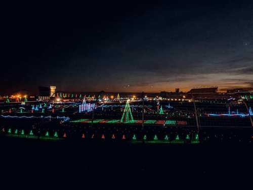 A vibrant display of colorful Christmas lights illuminates a landscape at dusk, featuring trees and festive decorations.