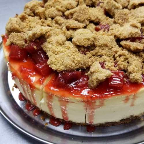 A delicious cheesecake topped with strawberry sauce and crumbled cookie pieces, sitting on a silver platter.