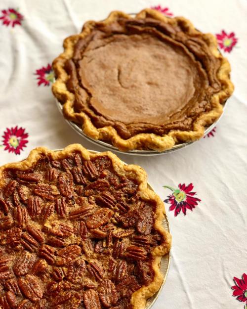 Two pies on a floral tablecloth: one pecan pie topped with nuts and one smooth, unbaked pie.