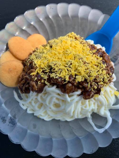 A bowl of noodles topped with a chocolate sauce and yellow sprinkles, accompanied by three cookies on the side.