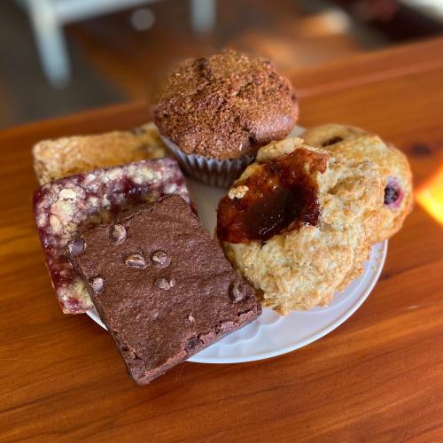A plate of assorted baked goods, including brownies, muffins, and pastries, arranged on a wooden table.