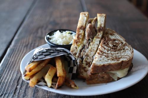 A hearty sandwich on toasted bread, served with fries and a side of coleslaw in a black bowl.
