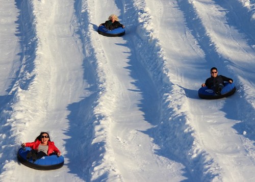 Three people slide down a snowy hill on inflatable tubes, enjoying a winter day.