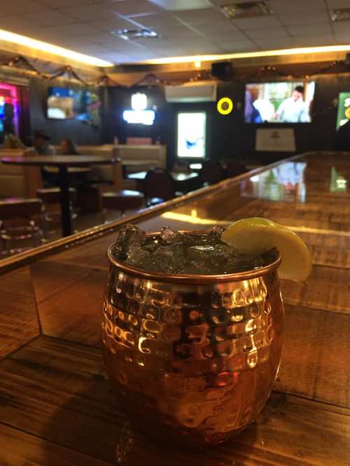 A copper mug filled with a cocktail and a lemon slice, set on a bar with a blurred background of a lively pub.