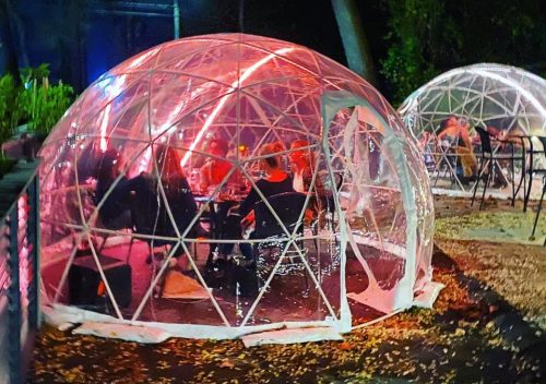 A cozy outdoor dining area with illuminated igloo-like structures surrounded by trees at night.