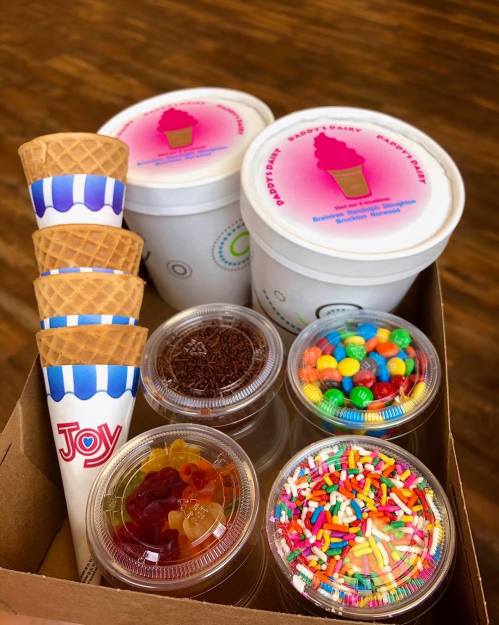 A box containing ice cream cups, waffle cones, and various toppings like sprinkles and candies.