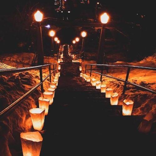 A snowy staircase illuminated by glowing lanterns on either side, creating a warm, inviting atmosphere at night.